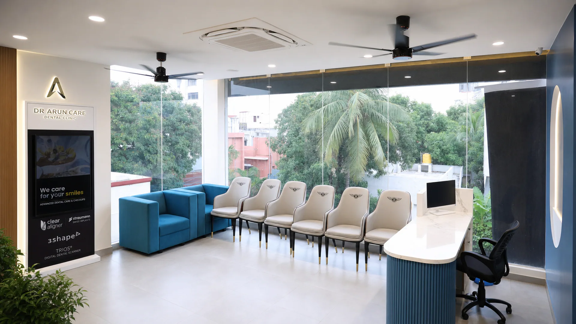 Waiting and reception area with white chairs, blue seating and full-height glazing overlooking trees.