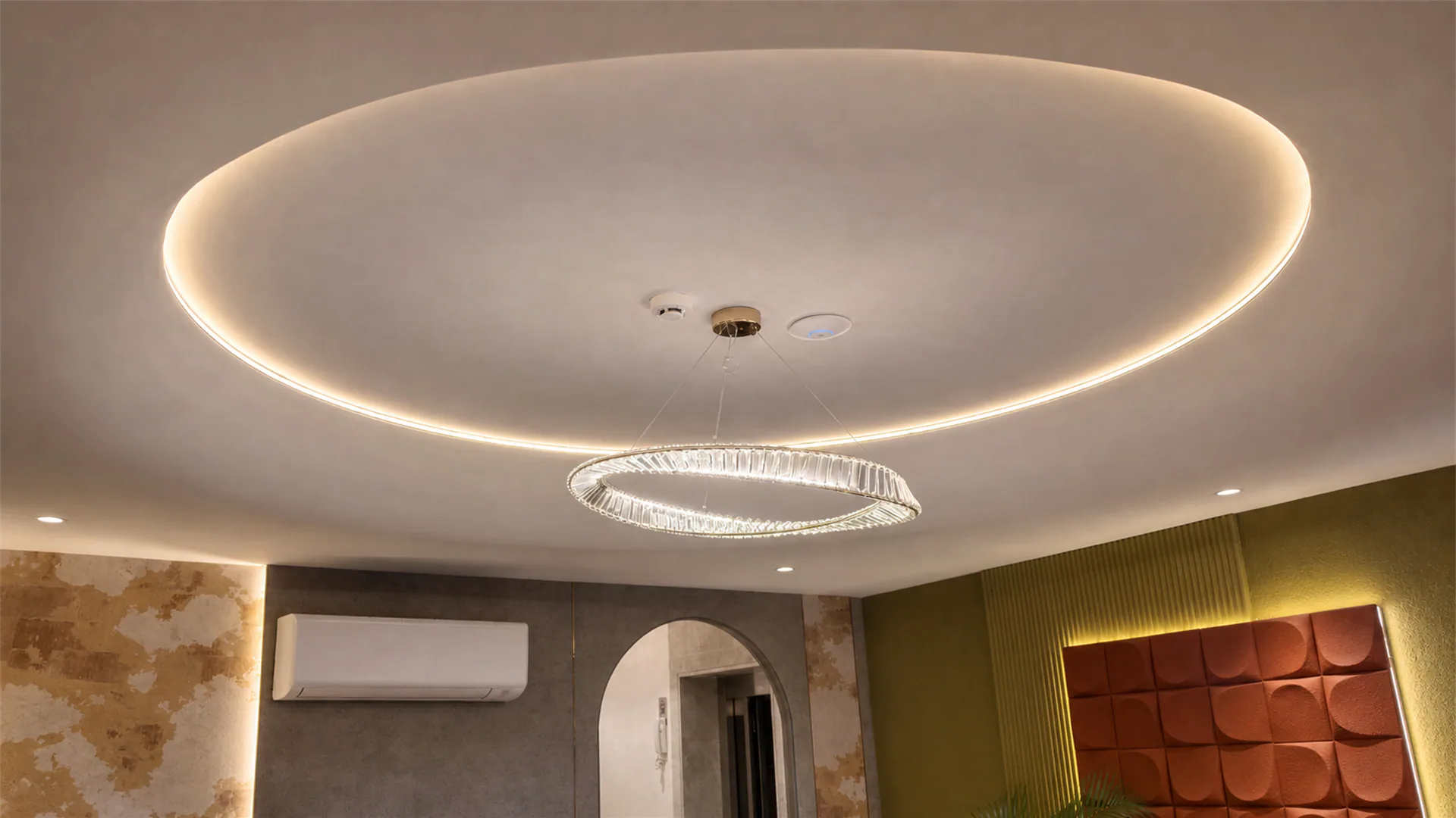 Residential room with a circular recessed ceiling light, central chandelier, arched doorway and upholstered wall panel.