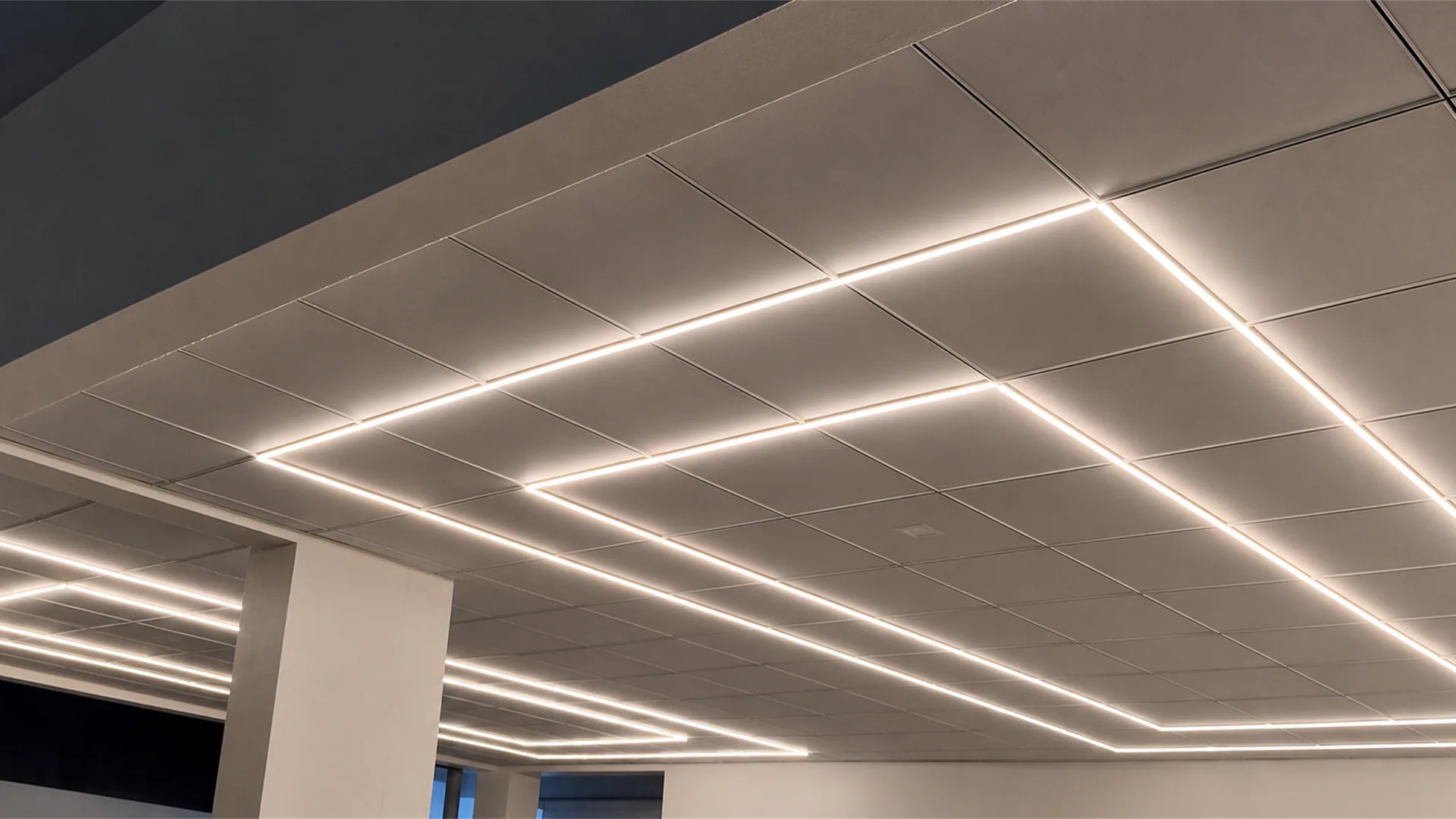 Close view of intersecting linear light strips set into a paneled ceiling above a column.