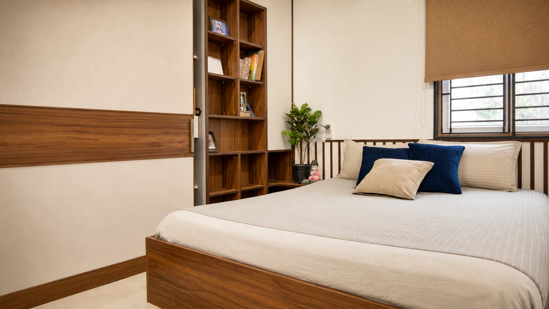 Bedroom with white bedding, blue cushion, open shelving and a window.