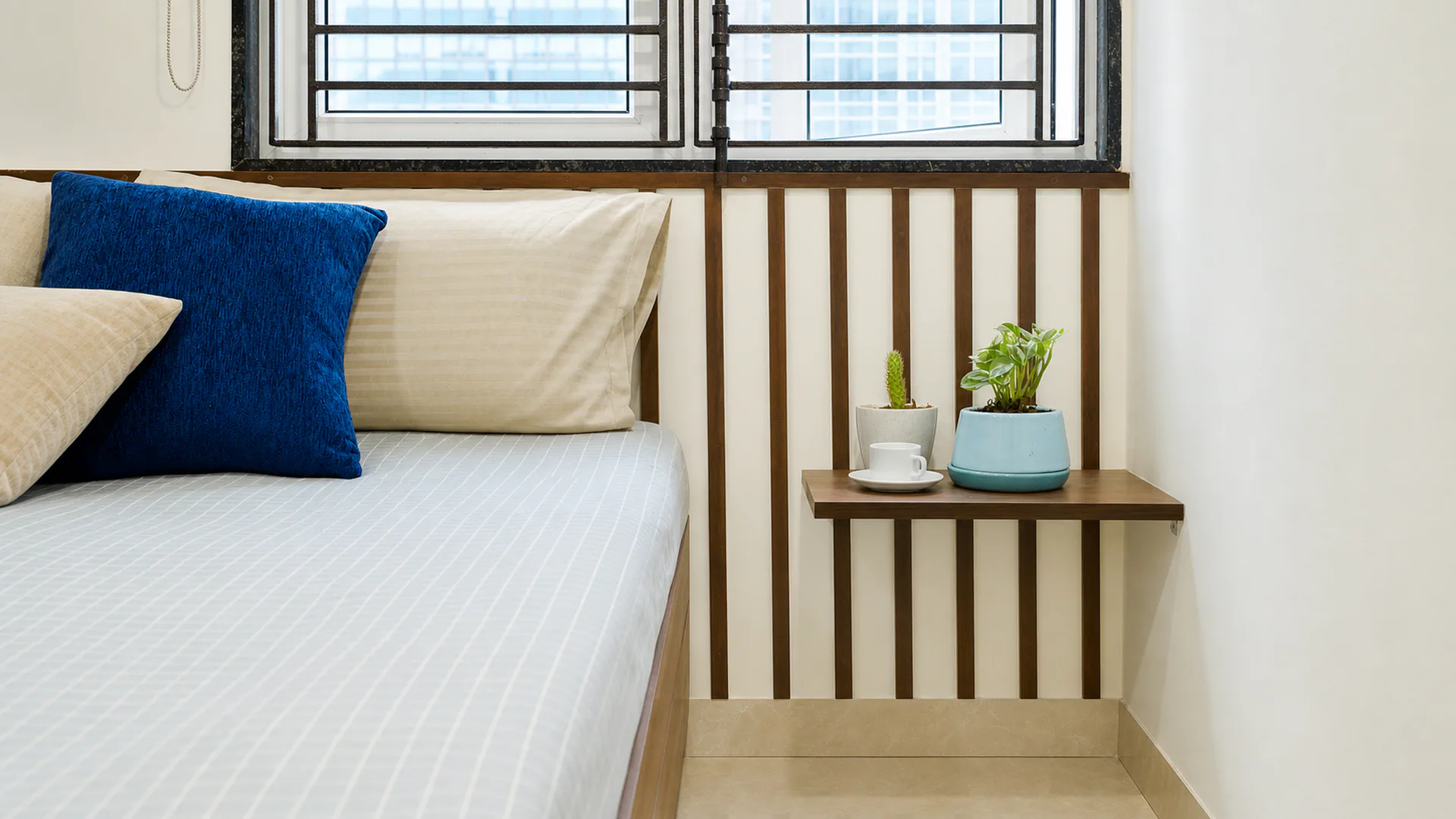 Close view of white bedding, a blue cushion and a small table beside a window.